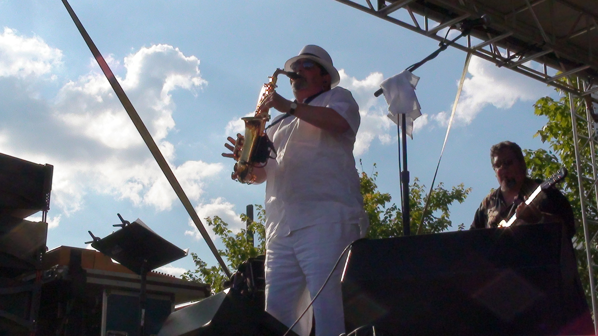 Bob Hunt in all white playing saxophone against a dramatic blue sky