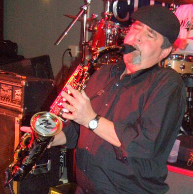 Bob Hunt playing saxophone bathed in red stage light at a club
