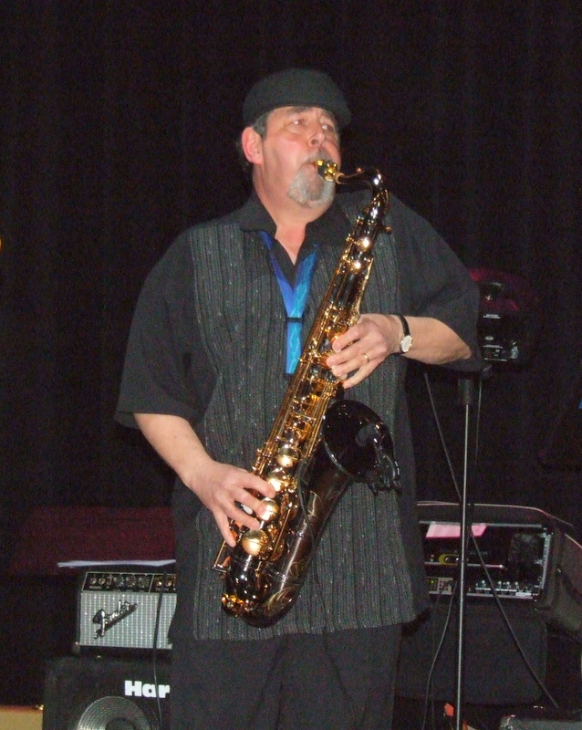 Bob Hunt playing a black-and-gold tenor saxophone on a dark stage