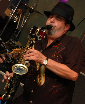 Intimate close-up of Bob Hunt in a flame-print shirt playing saxophone in warm club light