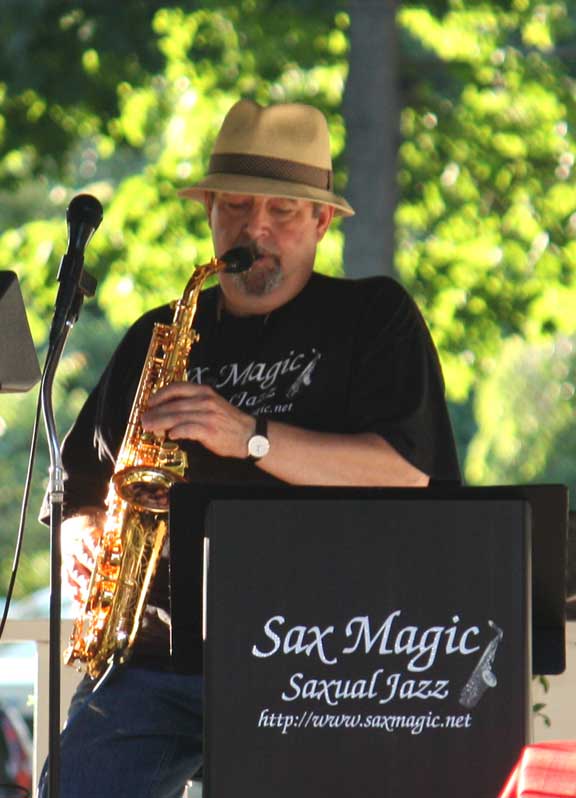 Bob Hunt in a Sax Magic tee playing gold saxophone behind the branded Sax Magic podium